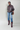 Woman wearing a brown leather jacket, blue jeans, and maroon boots on a plain background
