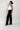 Woman wearing a white top and black pants against a plain background