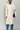 Woman wearing a beige trench coat and blue jeans against a plain background