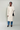 Woman wearing a beige trench coat with blue jeans and black shoes on a plain background