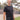 A tall and slim man standing outside. The model is wearing an extra long slim black henley shirt. The tall black henley shirt features a 3" longer body, 100% organic cotton, and is soft & preshrunk. The black henley shirt is ideal for tall slim men 6'2"+.