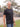 A tall and slim man standing outside. The model is wearing an extra long slim black henley shirt. The tall black henley shirt features a 3" longer body, 100% organic cotton, and is soft & preshrunk. The black henley shirt is ideal for tall slim men 6'2"+.