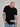 A tall athletic guy standing in a studio and wearing a black XL tall t-shirt, looking down at the Just Tall monogram logo.