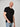 A tall and slim man in the studio standing in front of a light background with one hand in his pocket. The smiling model is wearing an extra long slim black v-neck t-shirt in a size XL. The tall black v-neck t-shirt features a 3" longer body, 100% organic cotton, and is soft & preshrunk. The black v-neck t-shirt is ideal for tall slim men 6'2"+.