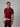 An upper body shot of a tall slim man standing and smiling in a studio and wearing a maroon medium tall polo shirt.