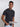 An upper body shot of a tall slim guy  in a studio and wearing a charcoal medium tall t-shirt, hand in pocket.