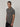 A tall and slim man in the studio standing in front of a light background. The smiling model is wearing an extra long slim dark grey polo shirt in a size medium. The tall dark grey polo shirt features a 3" longer body, 100% organic cotton, and is soft & preshrunk. The dark grey polo shirt is ideal for tall slim men 6'2"+.