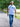A tall man walking on a gravel path in a park, wearing a white t-shirt with a colorful graphic print and blue jeans.