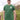 A tall and slim man standing by the sea. The smiling model is wearing a green extra long graphic t-shirt with the text tall club and a tree logo. It features a 3" longer body, 100% organic cotton, and is soft & preshrunk. This extra long tall graphic tee is ideal for tall slim men 6'2"+