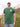 A tall and slim man standing by the sea. The smiling model is wearing a green extra long graphic t-shirt with the text tall club and a tree logo. It features a 3" longer body, 100% organic cotton, and is soft & preshrunk. This extra long tall graphic tee is ideal for tall slim men 6'2"+