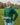 An upper body shot of a tall athletic guy standing in a park wearing a dark green extra long tall long sleeve t-shirt and showing  the Just Tall minimalist monogram logo.