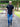 A tall man standing on a park path wearing a black fitted short-sleeve t-shirt and blue jeans, with text callouts describing the shirt's fit and length.