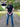A tall man standing on a park path viewed from behind, wearing a black fitted short-sleeve t-shirt and blue jeans. Text overlays highlight the product features: '100% Mercerised Organic Cotton Planet Friendly' with a fabric swatch circle, and 'Fitted Sleeves Skinny Arm Fit' with a pointer to the sleeve.