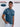 An upper body shot of a tall slim guy in a studio and wearing a petrol medium tall t-shirt, hand in pocket.