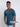 An upper body shot of a tall slim guy in a studio and wearing a petrol medium tall t-shirt, smiling and hand in pocket.