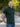 A tall and muscular man standing in a park, hands in back pockets and wearing a tall dark pine XL tall polo shirt.