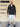 A head to toe shot of a tall slim guy standing in front of a beige wall, smiling and wearing an XL tall slim black zip up hoodie.