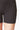 A close-up of a person wearing TLC Sport’s Extra Strong Compression Front Seam Micron Shorts with High Waisted Tummy Control in black, highlighting the lower torso and upper thighs against a white background.