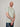 A tall and slim guy smiling in the studio, one hand grasping the other arm and wearing a sage green XL tall slim v-neck t-shirt.